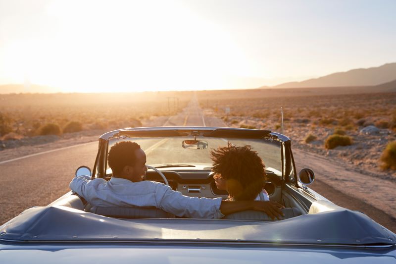 Ein liebevolles afroamerikanisches Paar fährt in einem offenen Cabrio in der Sommersonne. Erosscia ist Vergnügen neu gedacht